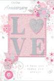 A romantic anniversary card is shown in close view, its design echoing the quiet intimacy of a shared evening at home in Wimbledon. The card is washed in soft pastel pinks and silvery greys, creating a gentle, almost velvety backdrop. At the centre sits the word LOVE, formed from slightly raised letters dusted with fine glitter, so the surface catches the light with a subtle sheen. The letter O is replaced by a shimmering heart, textured in silver and framed by the other letters like a jewel set within an elegant ring. Around this focal point, delicate illustrations of blossoms unfold in blush, mauve, and ivory tones, their edges softened as if painted in watercolour. The petals and leaves are drawn with flowing lines that curve and spiral, reminiscent of the natural rhythm of a florist's hand arranging stems on a bench just off Wimbledon High Street. Small, whimsical flourishes - tiny petals, swirling tendrils, and almost imperceptible butterflies - appear at the edges, giving the sense that the design is gently in motion, like flowers swaying in a light breeze across Wimbledon Common. The phrases On Our Anniversary and I love you today and always are written in a graceful, understated script, nestling comfortably amidst the floral artwork without overpowering it. Together, the raised glittered lettering, the heart motif, and the soft floral frame create the feeling of a treasured keepsake, as meaningful as a hand-delivered bouquet arriving at a doorstep in SW19. The card's overall mood is tender and heartfelt, designed to celebrate an enduring love story with quiet elegance.